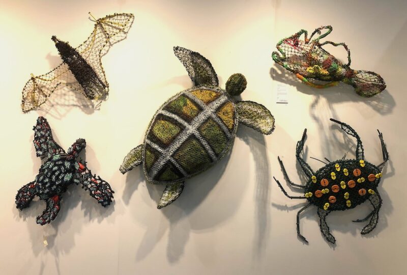 An exhibition wall of ghost-net works: turtle, crab, crocodile and fish